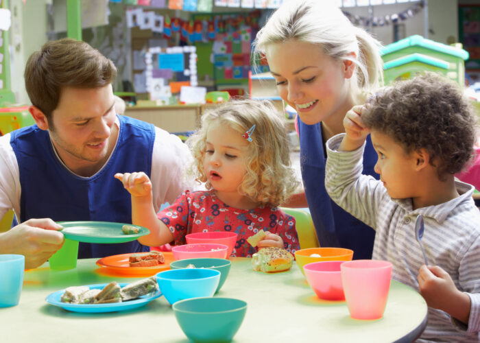 Une jeune femme et un jeune homme jouent autour d'une table avec des jeunes enfants dans une crèche.
